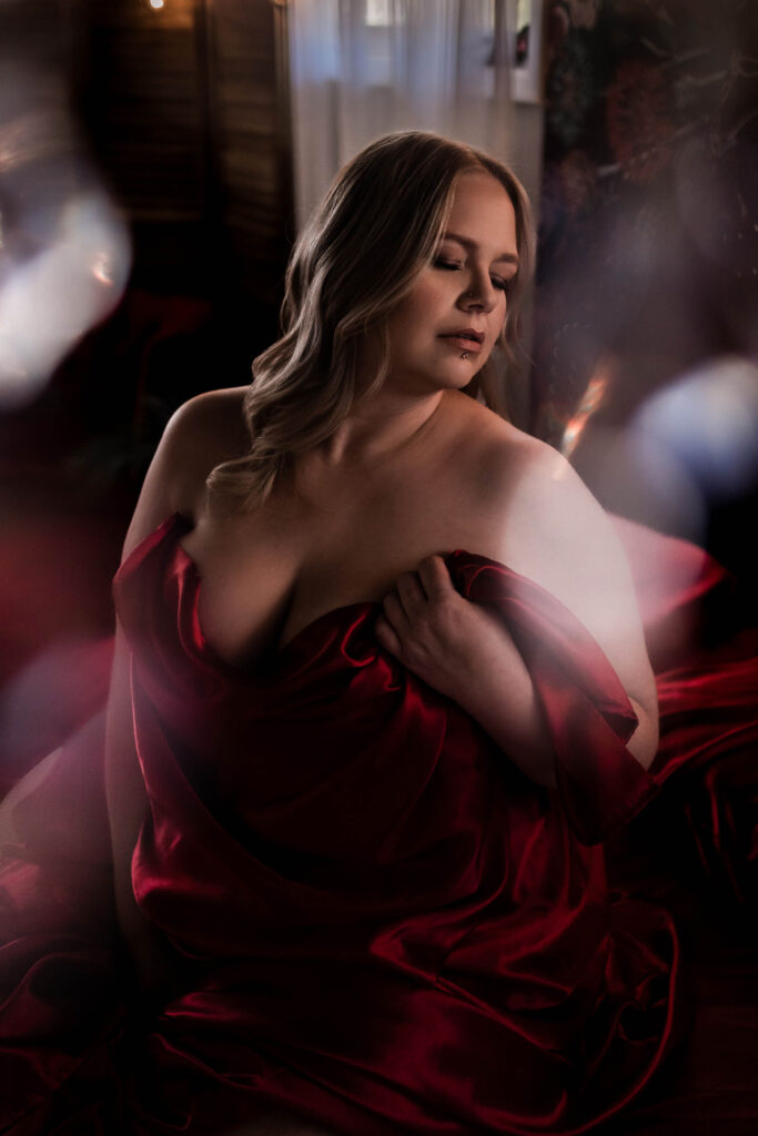 Boudoir photograph of woman drapped in red satin on a bed